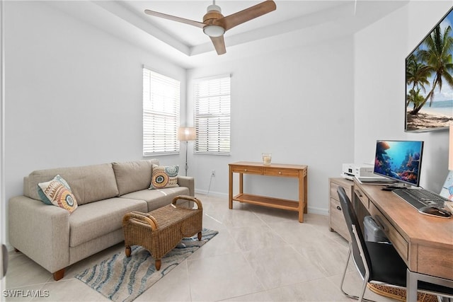 home office with light tile patterned floors, a raised ceiling, a ceiling fan, and baseboards