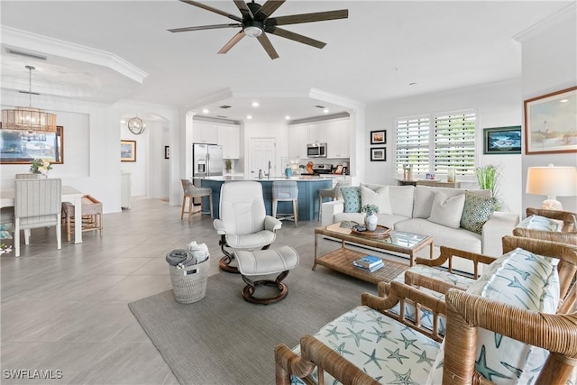 living area with light tile patterned floors, recessed lighting, ceiling fan with notable chandelier, visible vents, and crown molding