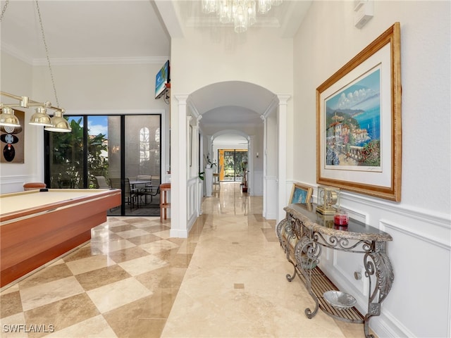 hallway featuring arched walkways, crown molding, a decorative wall, wainscoting, and ornate columns