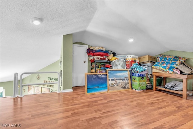 game room featuring vaulted ceiling, a textured ceiling, and wood finished floors