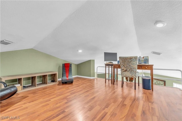 office area with a textured ceiling, wood finished floors, visible vents, baseboards, and vaulted ceiling