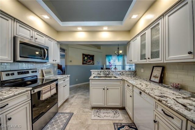 kitchen featuring stainless steel appliances, a peninsula, a sink, backsplash, and glass insert cabinets