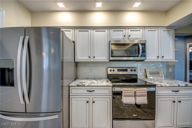 kitchen with appliances with stainless steel finishes, white cabinetry, backsplash, and light stone counters