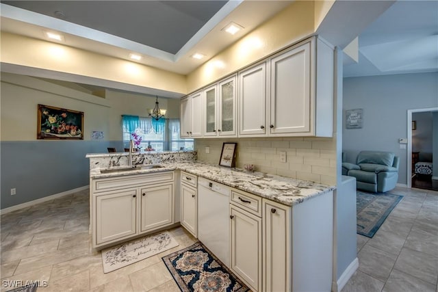 kitchen featuring white dishwasher, light stone countertops, a peninsula, a sink, and decorative backsplash