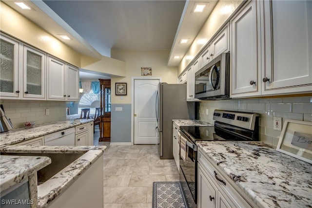 kitchen with appliances with stainless steel finishes, glass insert cabinets, and light stone countertops