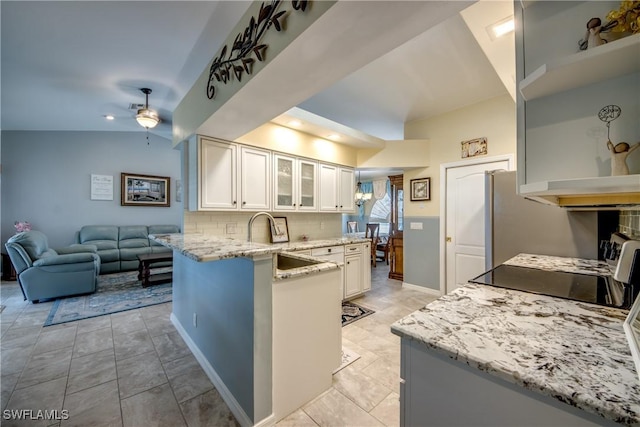 kitchen featuring decorative backsplash, a ceiling fan, glass insert cabinets, a peninsula, and light stone countertops