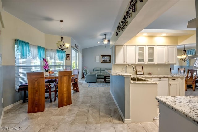 kitchen with lofted ceiling, light stone counters, a notable chandelier, a peninsula, and a sink