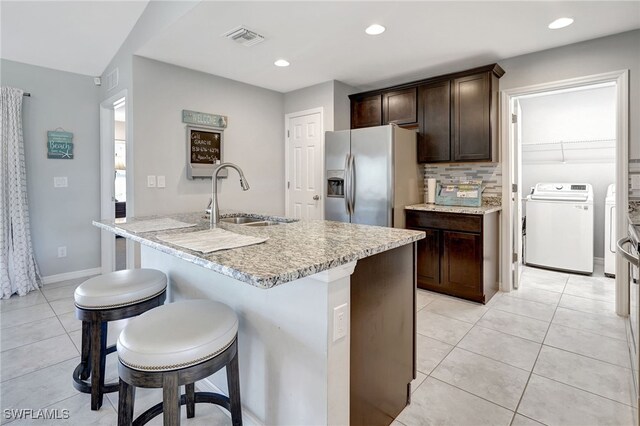 kitchen with visible vents, a sink, stainless steel refrigerator with ice dispenser, washer and dryer, and a kitchen bar