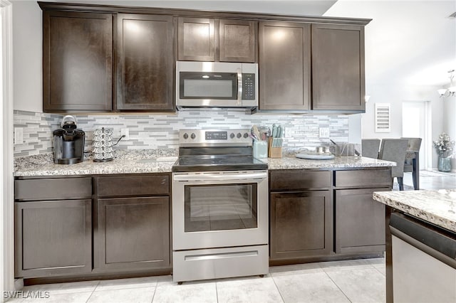 kitchen featuring tasteful backsplash, dark brown cabinets, stainless steel appliances, and light stone countertops