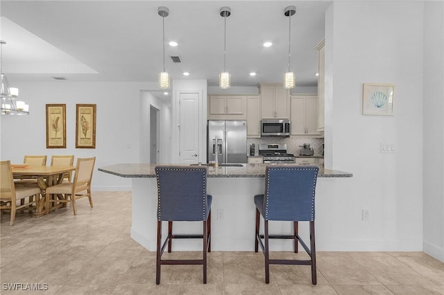 kitchen featuring dark stone countertops, a sink, stainless steel appliances, a kitchen bar, and backsplash