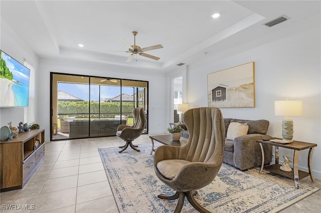 living area featuring light tile patterned floors, a tray ceiling, baseboards, and visible vents