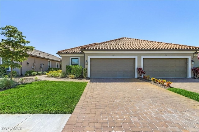 mediterranean / spanish-style home featuring a tiled roof, a front yard, stucco siding, decorative driveway, and an attached garage