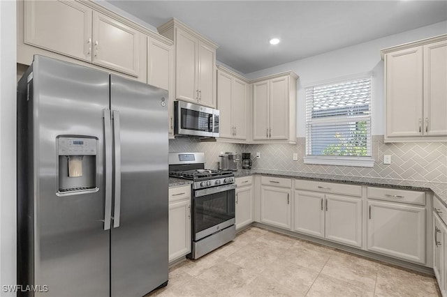 kitchen featuring dark stone countertops, stainless steel appliances, backsplash, and light tile patterned floors