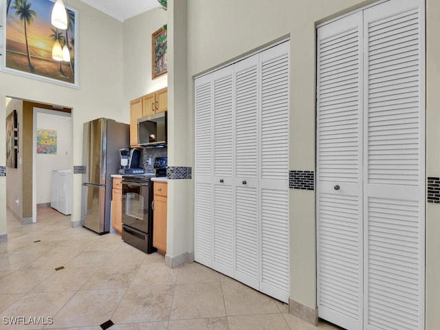 kitchen featuring light tile patterned flooring, light brown cabinets, stainless steel appliances, a high ceiling, and backsplash