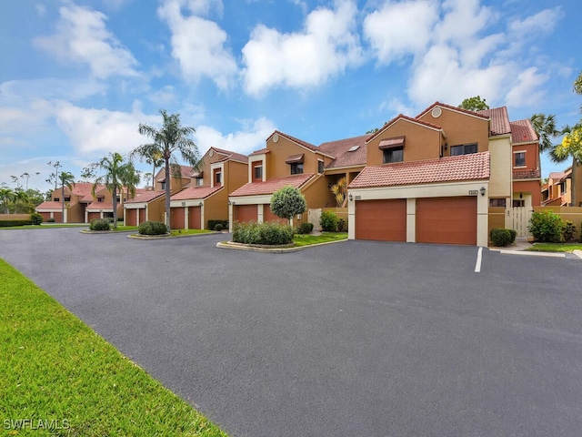 townhome / multi-family property with driveway, a tile roof, a residential view, and stucco siding