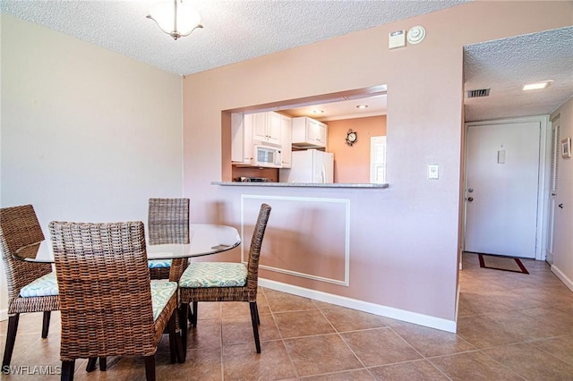 tiled dining space featuring baseboards, visible vents, and a textured ceiling