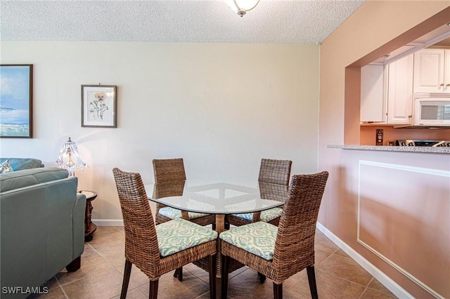 dining space with light tile patterned flooring, a textured ceiling, and baseboards