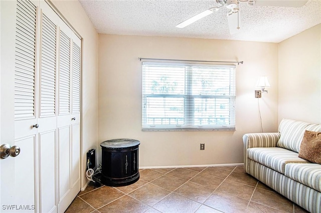 living area with tile patterned flooring, a ceiling fan, and a textured ceiling