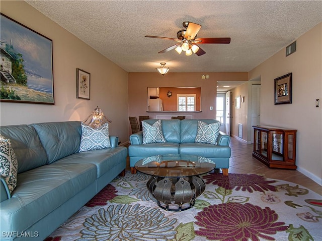 tiled living area with baseboards, a ceiling fan, visible vents, and a textured ceiling