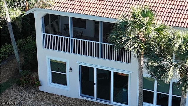 back of house featuring a sunroom, a tiled roof, and stucco siding