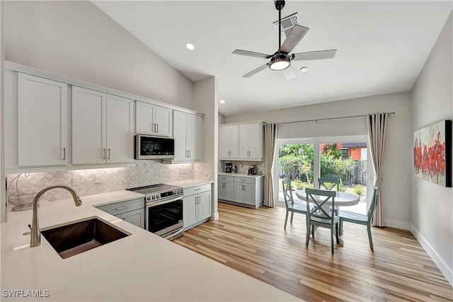 kitchen featuring light wood finished floors, tasteful backsplash, stainless steel appliances, light countertops, and a sink