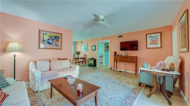 living room with baseboards, a textured ceiling, a ceiling fan, and wood finished floors