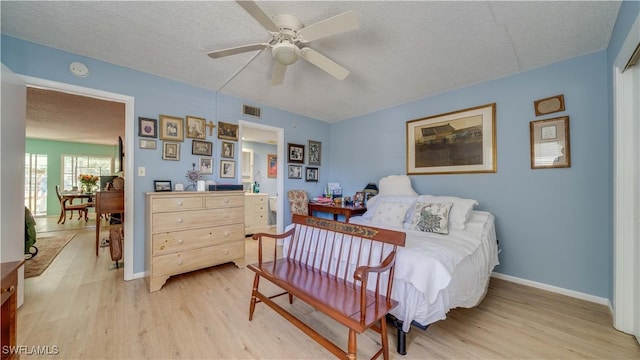 bedroom featuring a ceiling fan, baseboards, visible vents, light wood finished floors, and a textured ceiling