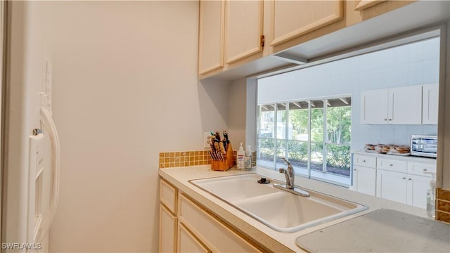 kitchen with a sink, stainless steel microwave, backsplash, and light countertops