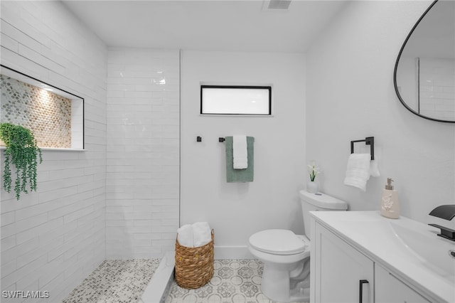 bathroom with visible vents, toilet, a tile shower, vanity, and baseboards