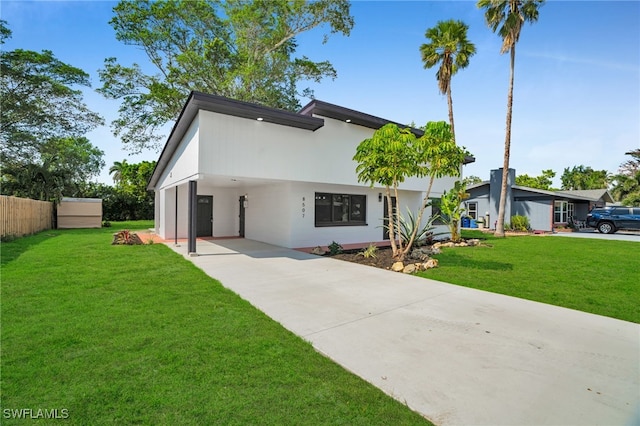 view of front of house featuring concrete driveway, a front lawn, fence, and stucco siding