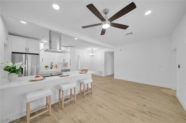 kitchen with white cabinetry, visible vents, stainless steel refrigerator, range hood, and a kitchen bar