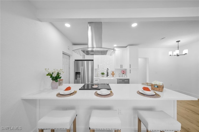 kitchen featuring a breakfast bar, stainless steel appliances, light countertops, island range hood, and a peninsula