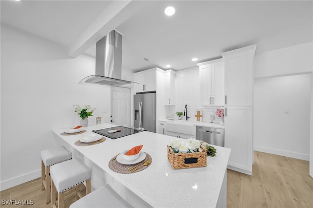 kitchen featuring white cabinets, a peninsula, island exhaust hood, stainless steel appliances, and light wood-type flooring