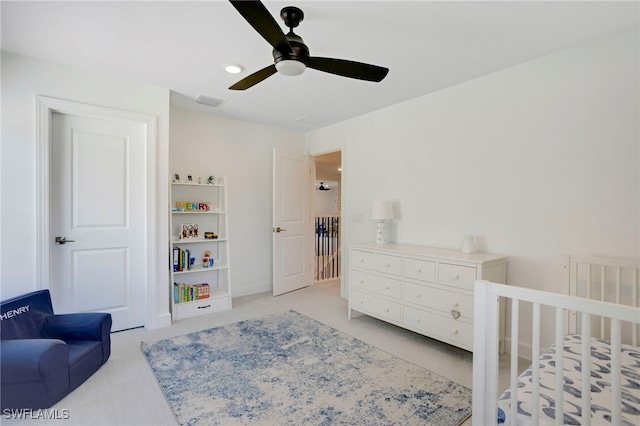 bedroom featuring a nursery area, light colored carpet, ceiling fan, and visible vents