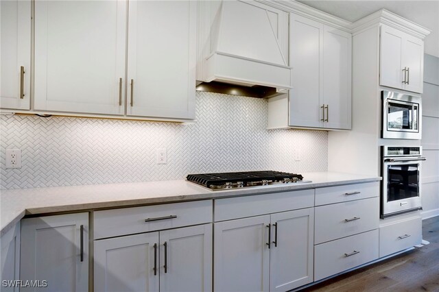 kitchen featuring tasteful backsplash, premium range hood, stainless steel appliances, and light countertops