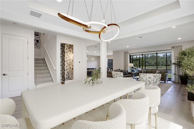 dining space featuring stairs, light wood finished floors, a raised ceiling, and visible vents