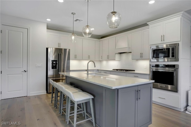 kitchen featuring premium range hood, a sink, visible vents, appliances with stainless steel finishes, and light wood finished floors