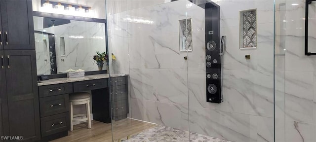 full bath with a marble finish shower, tile walls, and vanity