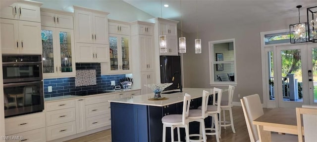 kitchen featuring black appliances, tasteful backsplash, light countertops, and a center island with sink