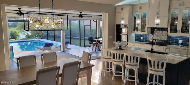 interior space with double wall oven, tasteful backsplash, light countertops, glass insert cabinets, and a sink