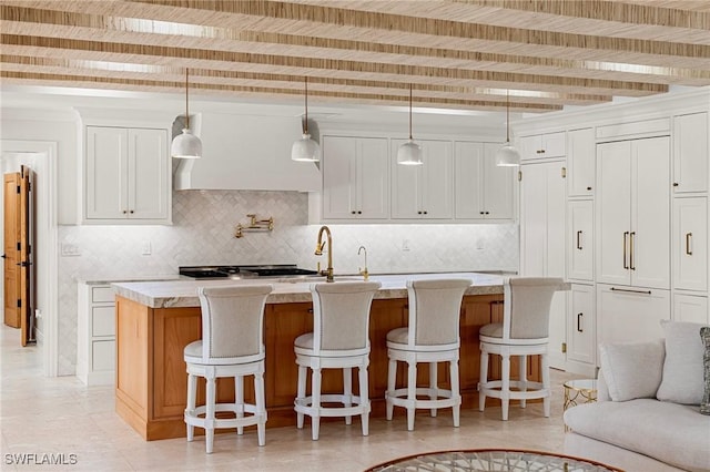 kitchen with beam ceiling, white cabinets, a center island with sink, and decorative backsplash