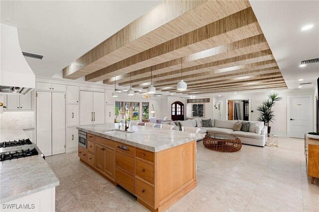 kitchen featuring open floor plan, stainless steel microwave, a sink, and light stone countertops