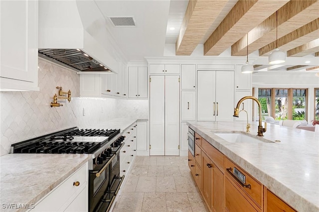 kitchen with visible vents, built in appliances, custom exhaust hood, stone tile flooring, and a sink