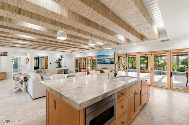 kitchen with stainless steel microwave, a sink, french doors, beamed ceiling, and stone tile flooring