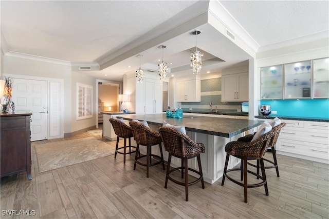 kitchen featuring visible vents, a breakfast bar area, a tray ceiling, decorative backsplash, and a sink