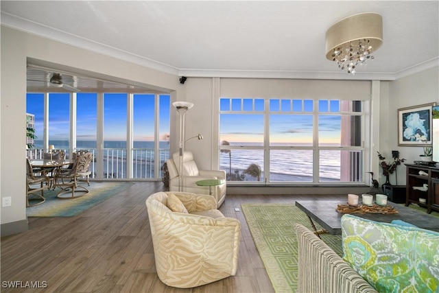 living room with wood finished floors, a chandelier, crown molding, and a water view