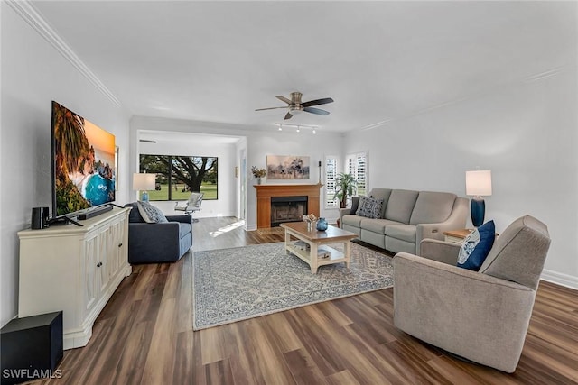 living area with a fireplace, a ceiling fan, baseboards, ornamental molding, and dark wood-style floors