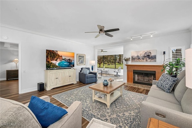 living area featuring ceiling fan, a fireplace, wood finished floors, baseboards, and crown molding