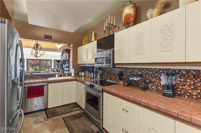 kitchen featuring stainless steel appliances, tasteful backsplash, visible vents, stone finish floor, and a sink