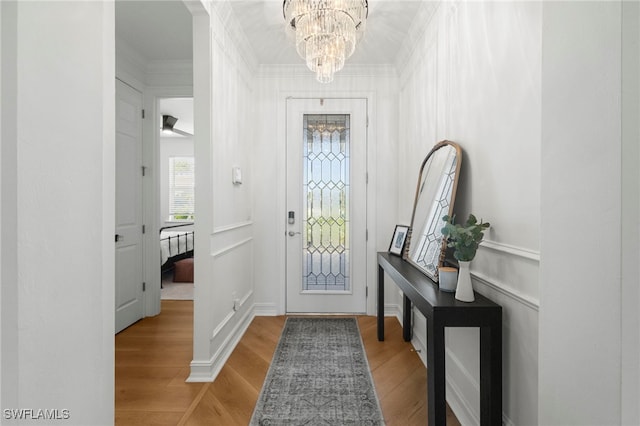 entryway with light wood-style floors, a chandelier, and crown molding